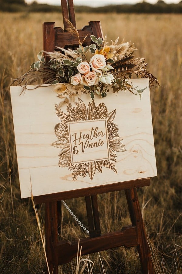 Laser cut timber welcome sign adorned with blush roses, feathers and dried foliage for wild bohemian wedding