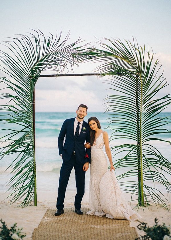 Palm fronds surround a beach wedding ceremony arch