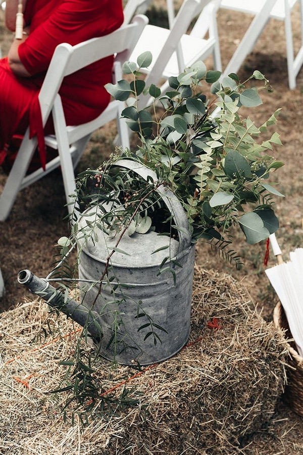 Rustic watering can filled with foliage on hay bales for outdoor boho wedding ceremony