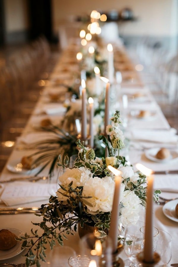 all white table setting features tall candlesticks + greenery