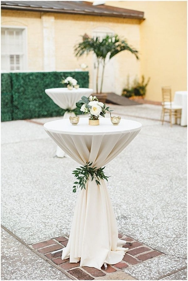 Neutral ivory wedding cocktail table with greenery leaves